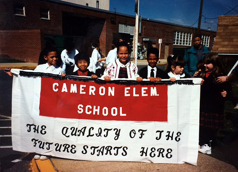 Color photograph of six students holding up a large red and white banner. The banner text reads, Cameron Elementary School, the Quality of the Future Starts Here.